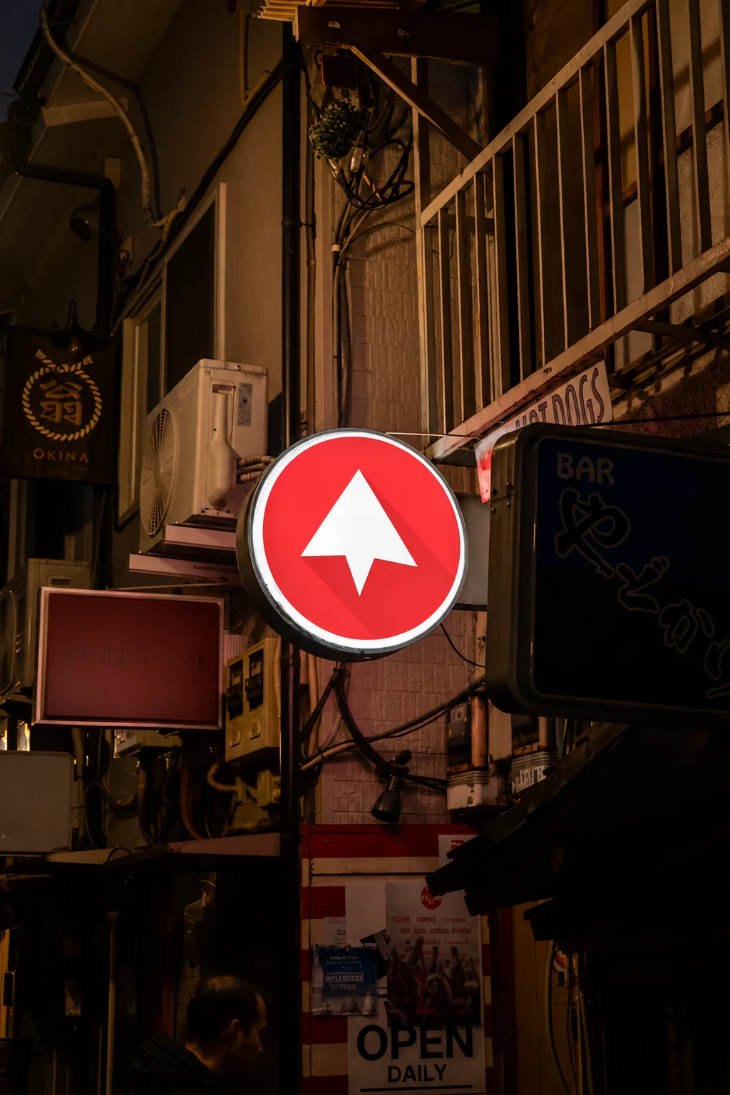 Placa circular iluminada com o símbolo da UPCOM em uma rua à noite